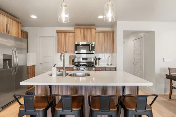 Kitchen featuring a center island with a built-in sink, stainless steel appliances, wood-finish cabinetry, and recessed lighting