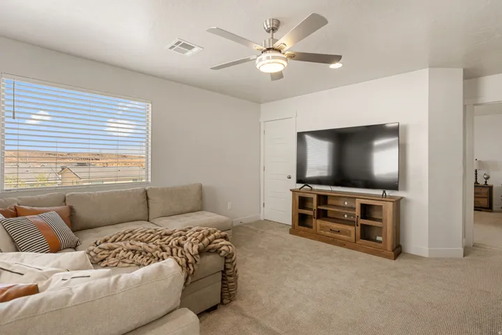 Spacious room featuring neutral carpet flooring, a large window with horizontal blinds, and a ceiling fan with integrated lighting
