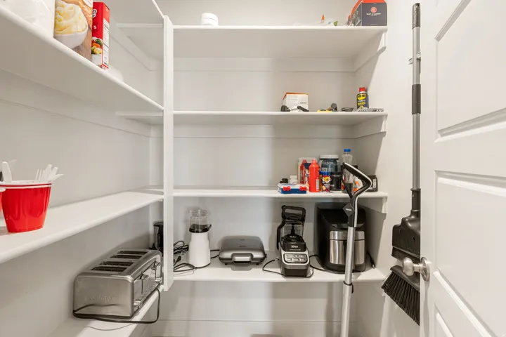 Utility pantry featuring white shelving, ample storage space, and a solid white door with a polished chrome doorknob