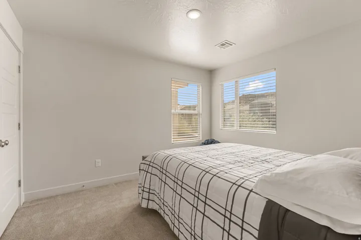Bedroom featuring light gray wall paint, two windows with blinds, and a neutral-toned carpet