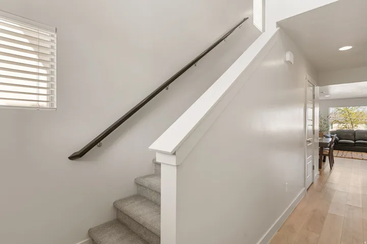 Carpeted staircase featuring a dark handrail and white balustrade, complemented by light wood-finish flooring