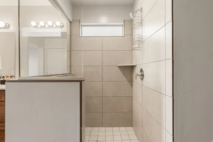 Spacious shower enclosure featuring light-toned large format tile, an integrated corner shelf, and a frosted transom window