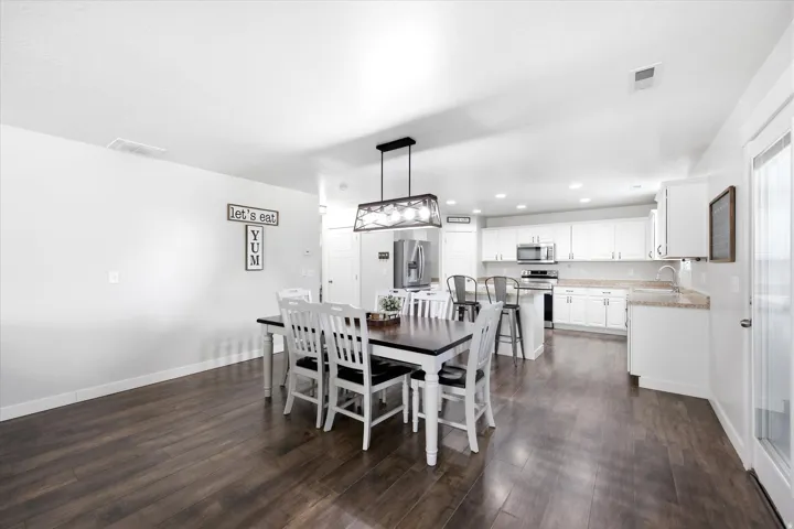 Spacious open-concept living area featuring dark wood-finish flooring, white walls, and a contemporary linear chandelier