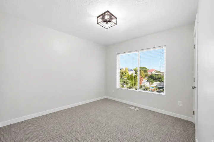 Bright room featuring a large window with horizontal blinds, neutral-toned carpet, light gray walls, white baseboards, and a modern flush-mount ceiling light fixture