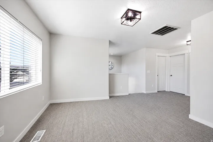 Spacious interior room featuring light gray carpeting, white baseboards, and a window with blinds