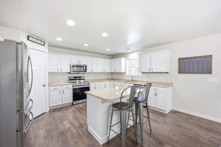 Bright kitchen featuring white cabinetry, light-colored countertops, stainless steel appliances, a central island, and wood-finish flooring