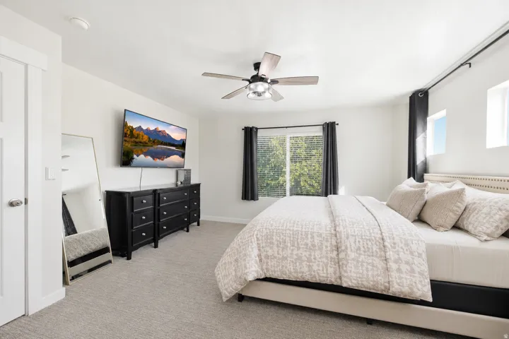 Spacious room featuring light gray carpeting, a ceiling fan with integrated lighting, and multiple windows with blinds
