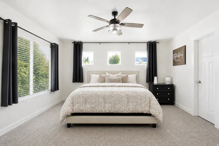 Carpeted bedroom featuring multiple window placements, a ceiling fan with integrated lighting, and a paneled interior door