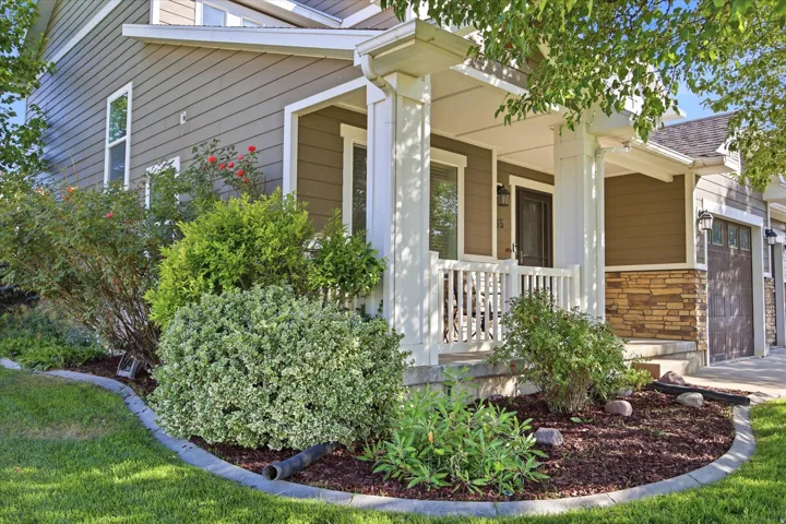 Front exterior featuring a covered porch with white railings, stone veneer accents, wood-finish garage doors, horizontal siding, and landscaped shrubbery with mulch beds