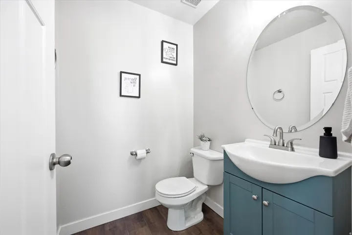 Powder room featuring a single-sink vanity with a blue base cabinet, a white oval basin, and a circular wall mirror