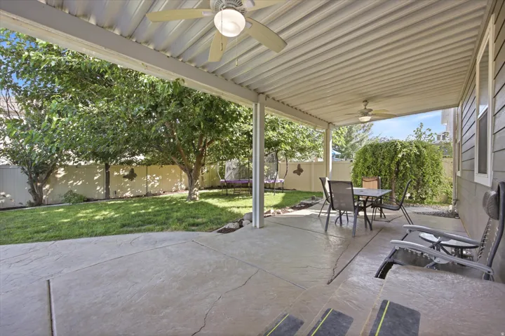 Expansive covered patio with corrugated metal roof and concrete flooring overlooking a mature landscaped yard featuring established trees, manicured lawn, and defined hardscape elements