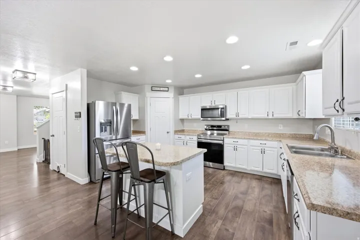 Modern kitchen featuring white cabinetry, stainless steel appliances, an island with countertop seating, wood-finish flooring, and recessed lighting