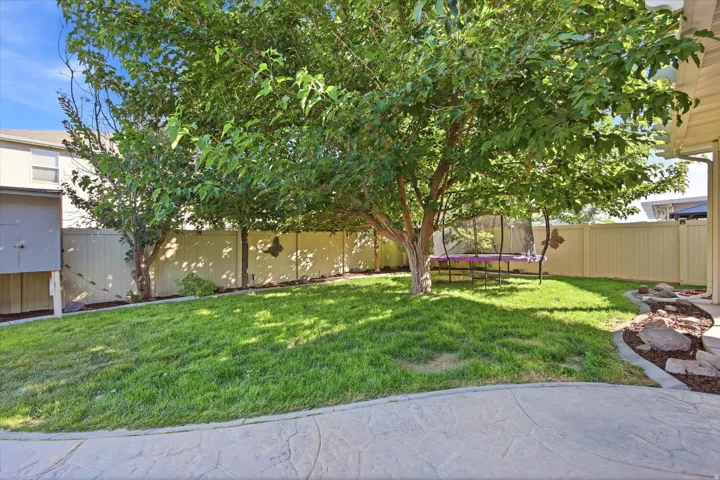 Fenced backyard featuring mature trees, a manicured lawn, stamped concrete patio, and a rock garden area