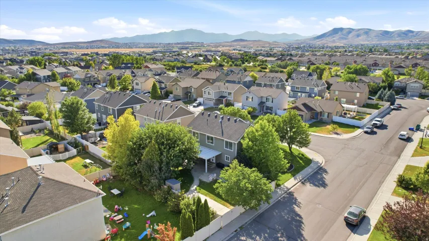 Aerial perspective of a developed residential area with mountain backdrop, showcasing single-family homes with pitched roofs, mature landscaping, and paved streets