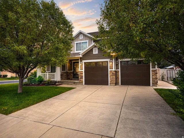 Two-story residence featuring a covered front porch with white railing, stone accents on the facade, and a two-car garage with dark wood-look doors