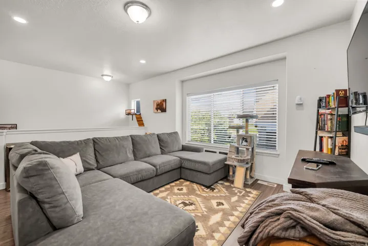 Spacious living area featuring neutral wall tones, recessed lighting, a large window with blinds, and wood-finish flooring