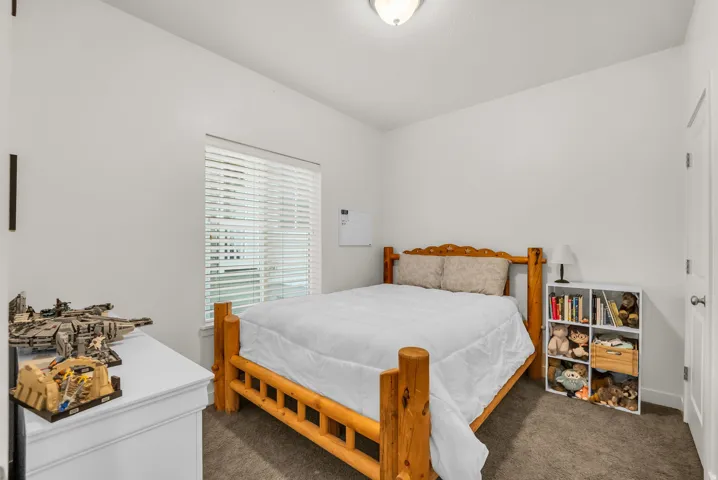 Bedroom featuring a single window with blinds, neutral-toned carpeting, white walls, and a ceiling-mounted light fixture