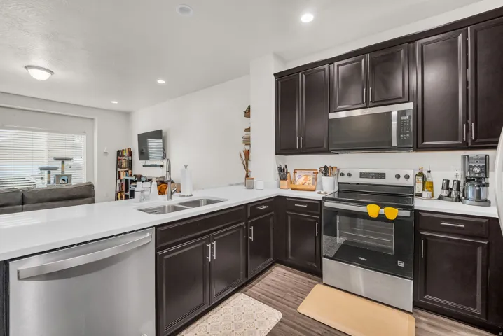 Modern kitchen featuring dark wood cabinetry, white countertops, stainless steel appliances, and wood-finish flooring
