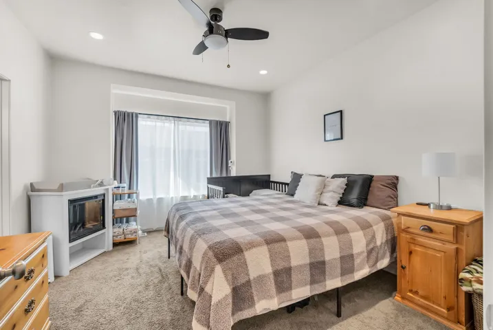 Carpeted bedroom featuring a large window with sheer and blackout blinds, recessed lighting, and a ceiling fan