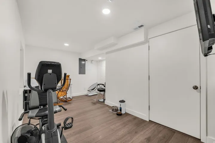 Finished basement space featuring wood-finish flooring, white walls, recessed lighting, and a white door with a round knob