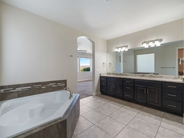 Bathroom featuring a corner soaking tub with tile surround, double vanity with dark wood-finish cabinetry, light-toned countertop, and dual mirrors with vanity lighting