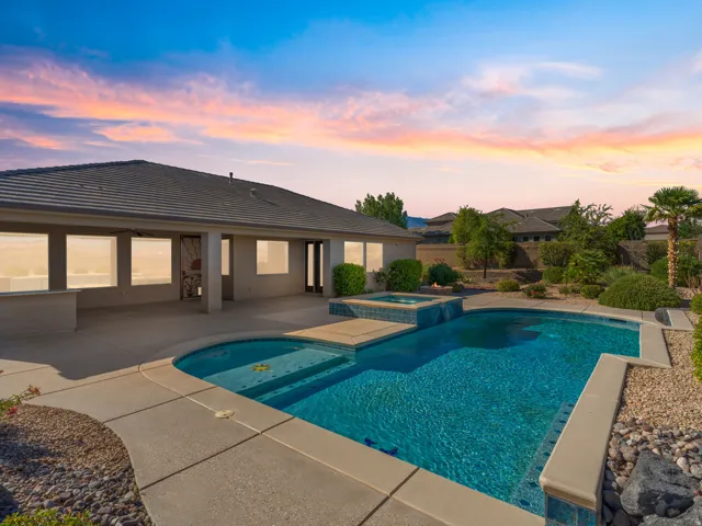 Backyard oasis featuring a sparkling blue swimming pool with integrated spa, expansive concrete patio, and low-maintenance landscaping