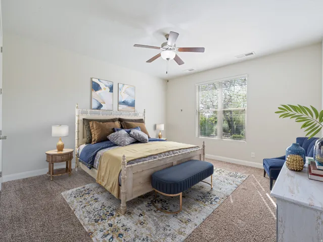 Carpeted bedroom featuring a large window with blinds, a ceiling fan with integrated lighting, and neutral wall tones