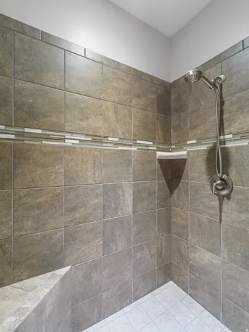 Tiled shower enclosure featuring a mosaic accent band, brushed nickel shower head and controls, a corner niche, and a built-in bench