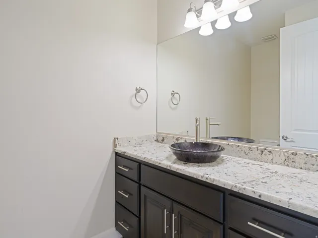 Bathroom vanity featuring a vessel sink, dark wood-finish cabinetry, a light-toned speckled countertop, and a large wall mirror with overhead light fixture