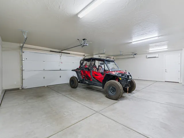 Spacious garage featuring a concrete floor, bright overhead strip lighting, white insulated garage door, and a white side entry door