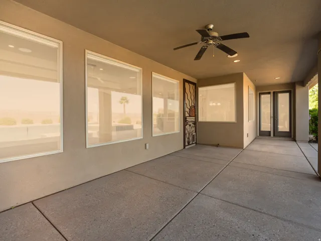 Spacious covered patio featuring concrete flooring, multiple large windows, and a ceiling fan with integrated lighting