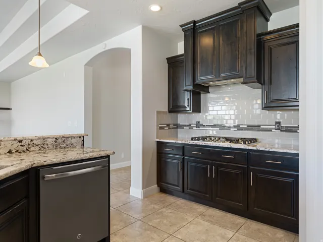 Kitchen featuring dark wood cabinetry, light-toned granite countertops, and a subway tile backsplash