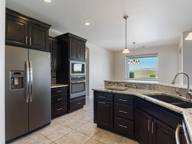 Kitchen featuring dark wood cabinetry, granite countertops, built-in stainless steel appliances, and tile flooring