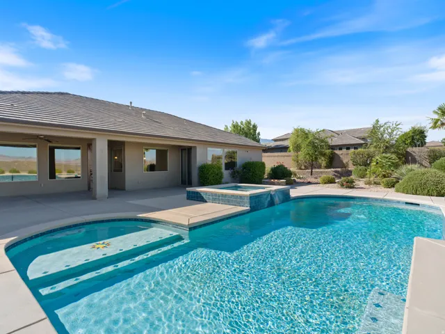 Expansive backyard oasis featuring a large inground swimming pool with integrated steps, an elevated spa with blue tile accents, and a wide perimeter of concrete decking