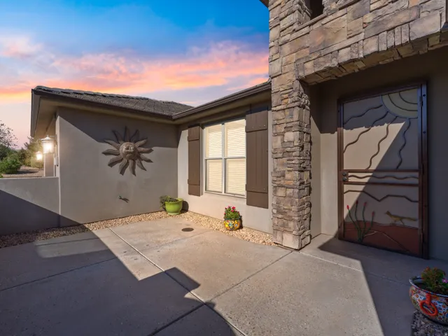 Stucco exterior featuring a stone facade accent, decorative security door, exterior lighting, and a window with functional shutters