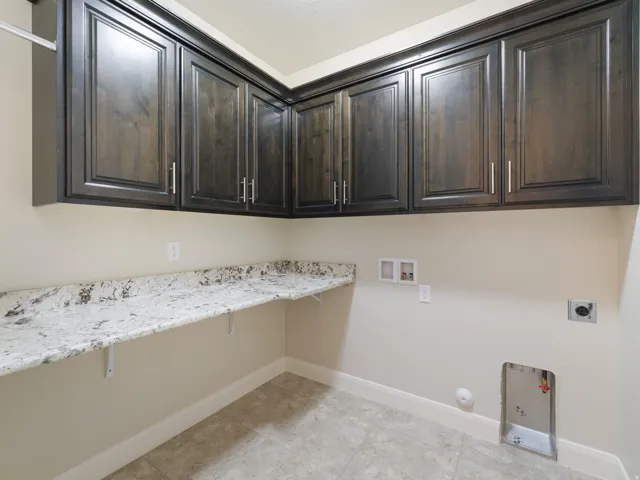 Laundry room featuring dark wood cabinetry, a light granite countertop, tile flooring, and a chrome hanging rod