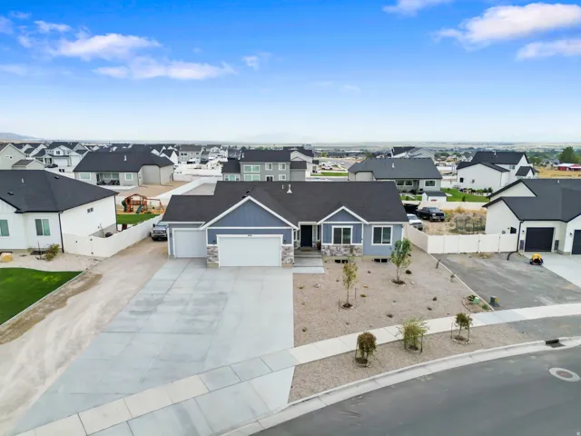 Ranch-style residence featuring a light blue siding exterior with stone accents, a dual-bay garage, a concrete driveway, and a paved sidewalk