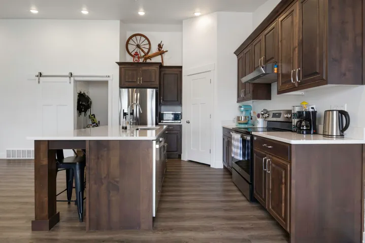 Open-concept kitchen featuring dark wood-finish cabinetry, a large kitchen island with counter seating, stainless steel appliances, and wood-finish flooring