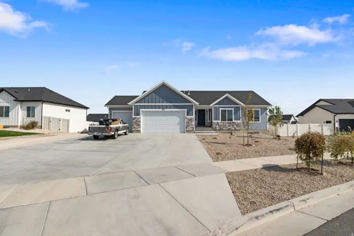 Blue siding exterior with stone accents, attached two-car garage, concrete driveway, and front yard landscaping with young trees