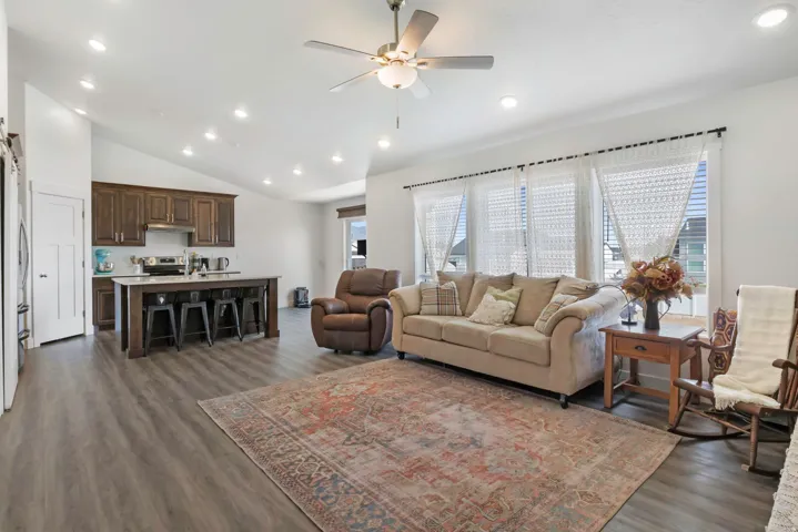 Open-concept living area with vaulted ceilings, recessed lighting, wood-finish flooring, and a kitchen featuring dark wood cabinetry and a central island
