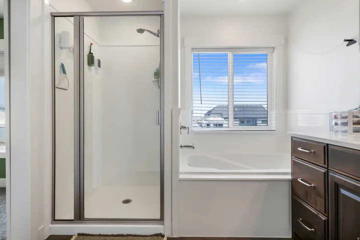 Glass-enclosed shower with a showerhead, a separate built-in bathtub with a window, and wood-finish cabinetry with a light-toned countertop