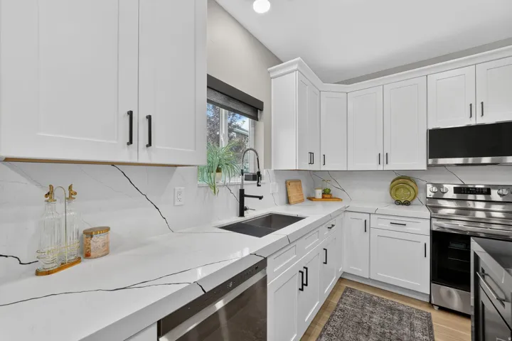 Modern kitchen featuring white shaker-style cabinetry with black hardware, white countertops and backsplash with dark veining, an undermount sink with a black faucet, and stainless steel appliances