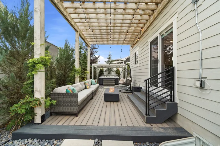Spacious outdoor deck featuring a wood pergola with string lights, composite decking, and a built-in hot tub under a separate pergola