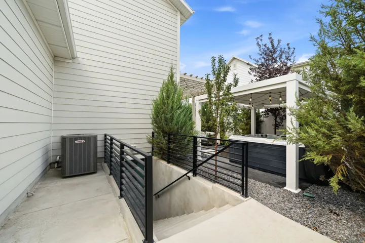 Exterior showcasing a hot tub beneath a white pergola with string lighting, a concrete patio, and mature landscaping