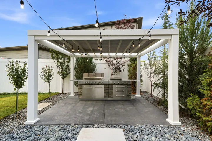 Outdoor entertaining area featuring a white pergola, string lighting, and a built-in grill station with stone accents