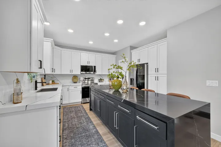 Kitchen featuring white shaker cabinetry, stainless steel appliances, a large center island with a dark countertop, wood-finish flooring, and recessed lighting