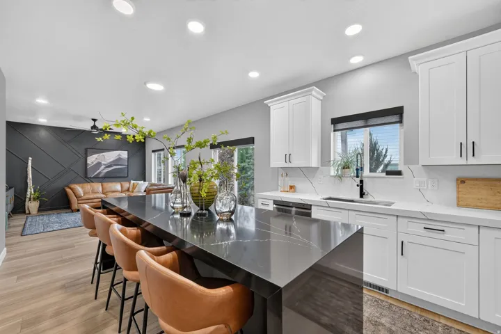 Open-concept living space featuring a substantial kitchen island with seating, white shaker cabinetry, light countertops with a subtle vein pattern, and recessed lighting