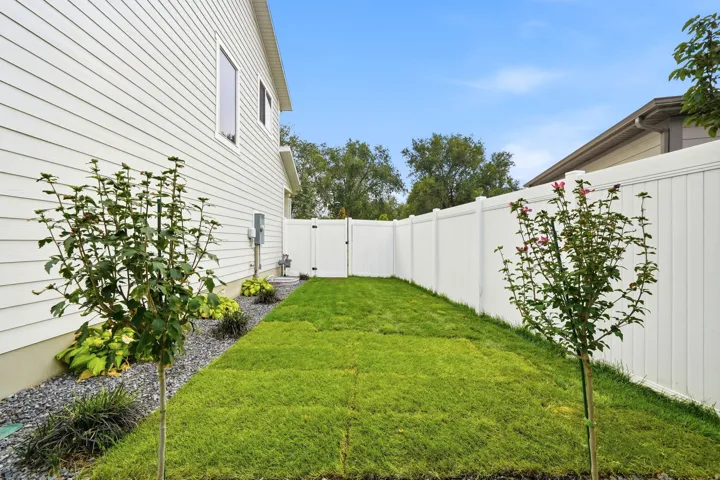 Grassed backyard area featuring a white vinyl fence, gravel landscaping, and mature plantings