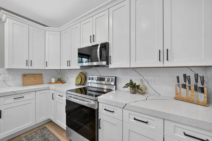 Modern kitchen featuring white shaker cabinetry with black hardware, stainless steel appliances, and light countertops with contrasting veining