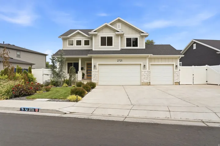 Light-toned siding exterior with stone accents, a three-car garage, and a concrete driveway